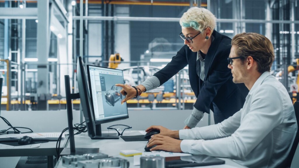 Zwei Automobil-Ingenieure diskutieren Concept Car Blueprints auf Desktop-Computer in modernen Büros in Montagewerken. Female Industrial Project Manager spricht bei der Fahrzeugfabrik mit dem männlichen Designer. (2076774058) - shutterstock.com
