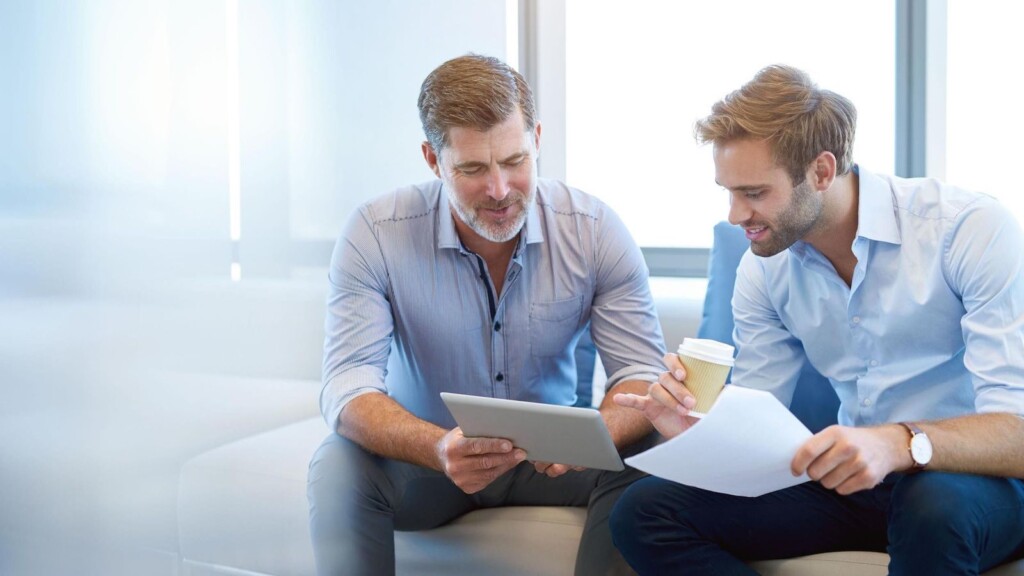 Praktischer, ausgereifter Geschäftsführer, der mit einem digitalen Tablet etwas Positives mit einem jungen Mitarbeiter in einer modernen Business Lounge diskutiert (446643169) - shutterstock.com